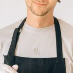 Styling - A Man in Black Apron Smiling while Holding a Plastic Bowl