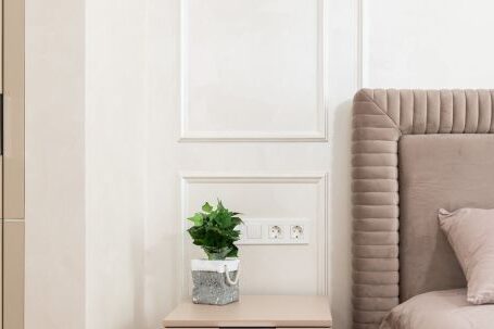 Wardrobe Essentials - Bedside table with potted plant placed near comfortable bed with pink coverlet and pillows in cozy room at home